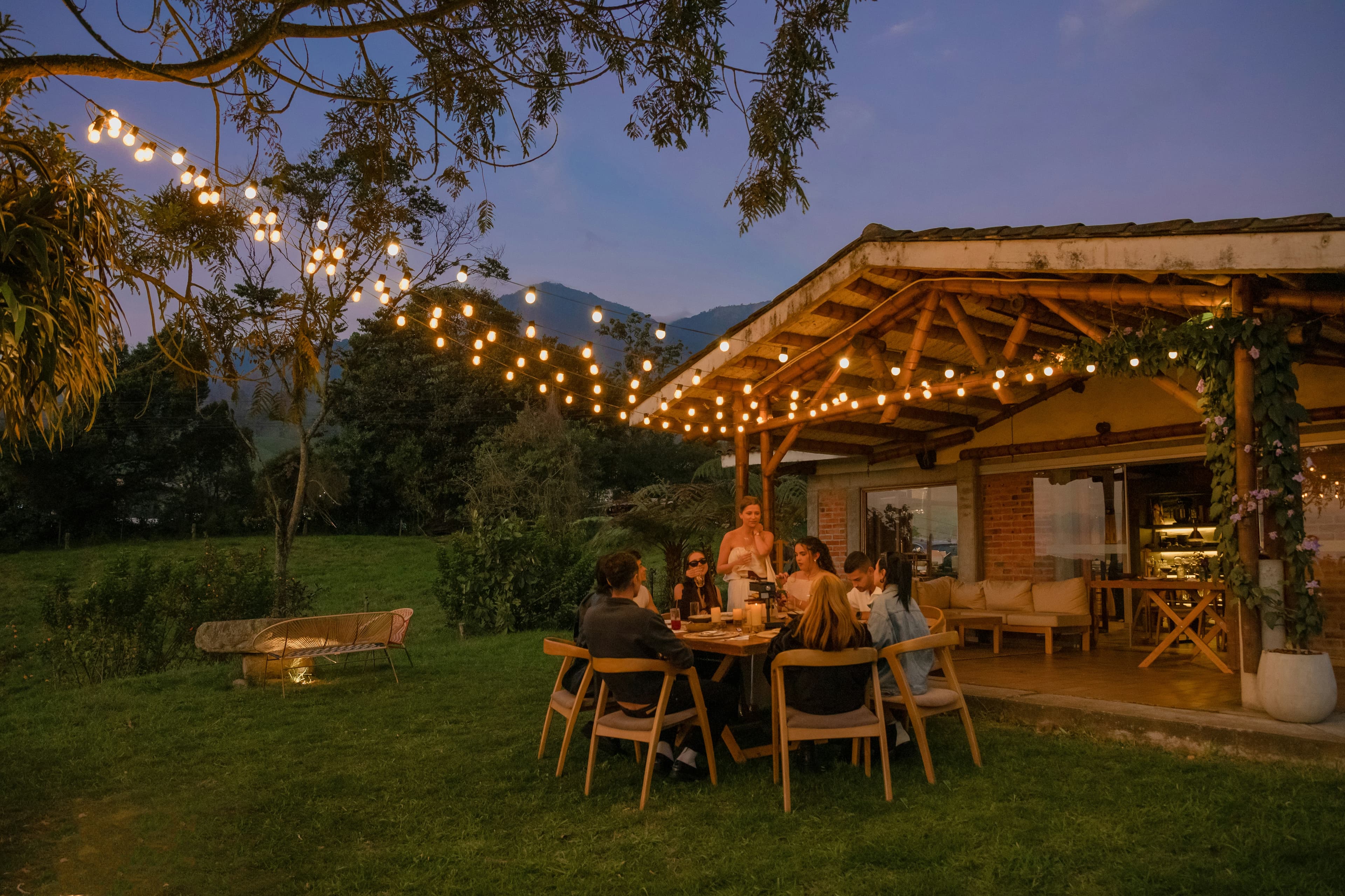 Friends gathered for a private chef dinner at a mountain home at dusk, lit by string lights